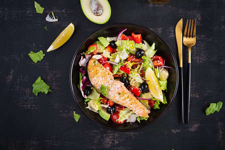 Baked salmon fish fillet and fresh green lettuce, tomato, avocado and black olives. Greek salad. top view.の写真素材