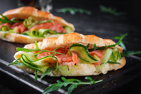 Croissants with salted salmon, cucumber and arugula served on dark background. close up.の写真素材