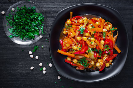 Vegetable stew of chickpeas, carrot, sweet peppers, onions, garlic and tomato sauce with lemon on the dark table. Oriental cuisine. top viewの写真素材