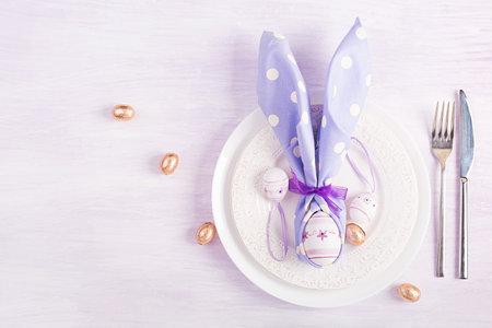 Easter table setting. White plate with a napkin folded in the shape of a rabbit, Easter and chocolate eggs on a pink background. Happy Easter holiday concept. top view, flat layの写真素材