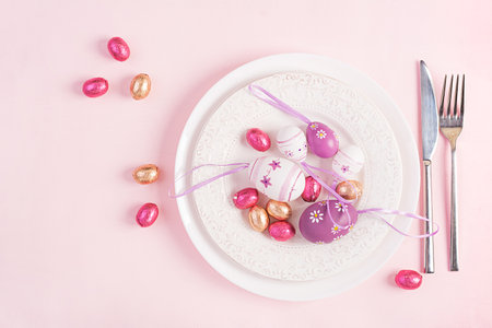 Happy Easter. Table setting for Easter holiday. Easter eggs, flower and cutlery on pink background....