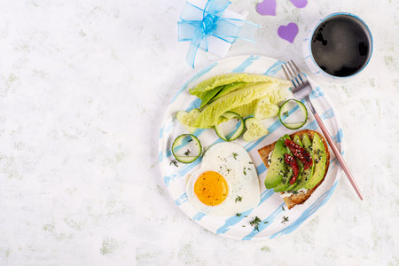Romantic breakfast for Valentine's Day. Fried egg and toast with avocado and cream cheese. Top viewの写真素材