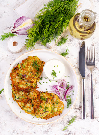 Zucchini fritters with red onions, garlic and herbs. Vegetarian zucchini pancakes and sour cream on white table. Top viewの写真素材