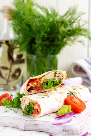 Grilled tortilla wraps with chicken and fresh vegetables on white wooden board. Chicken burrito....