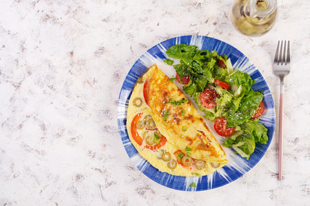 Omelette with tomatoes, green olives and fresh salad on blue plate. Frittata - Italian omelet. Top...