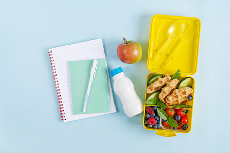 Kids lunch box with zucchini waffles, cucumber, cherry tomatoes and blueberries. Back to school breakfast background. Copy space. Top view, flat layの写真素材