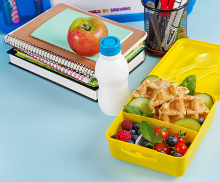 Kids lunch box with zucchini waffles, cucumber, cherry tomatoes and blueberries. Back to school breakfast background. Copy space. Top view, flat layの写真素材