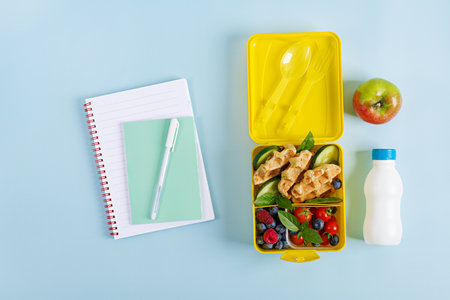 Kids lunch box with zucchini waffles, cucumber, cherry tomatoes and blueberries. Back to school breakfast background. Copy space. Top view, flat layの写真素材