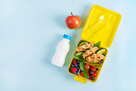 Kids lunch box with zucchini waffles, cucumber, cherry tomatoes and blueberries. Back to school breakfast background. Copy space. Top view, flat layの写真素材
