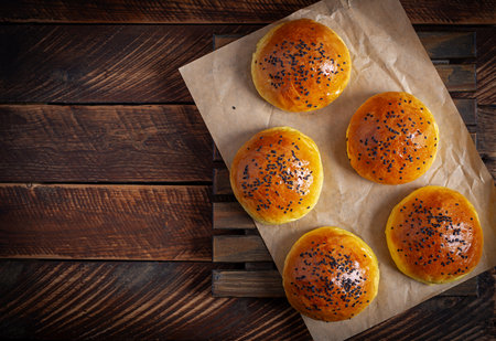Homemade freshly baked plain golden brown soft hamburger buns topped with sesame seeds against wooden background.の写真素材