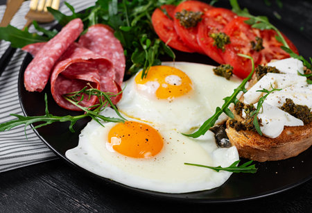 English breakfast. Fried eggs, salami, tomatoes and toast with feta and pesto.の写真素材