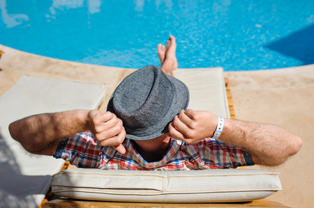 Man in a hat lying on a lounger by the pool.の写真素材