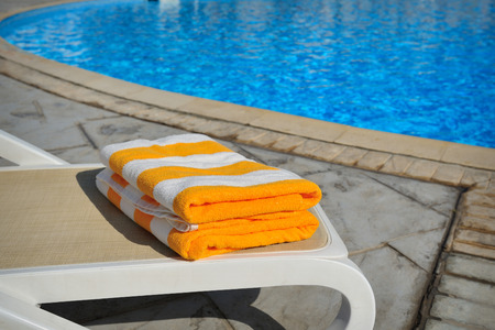 Two yellow striped towels lie on a sun-bed near a swimming pool.の写真素材