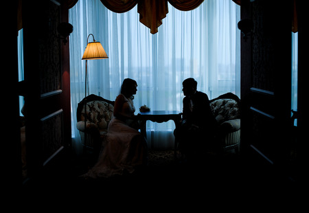 bride and groom in silhouette sitting opposite each other.の写真素材