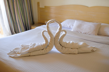 Tucked bed with swans out of towels in a hotel room.の写真素材