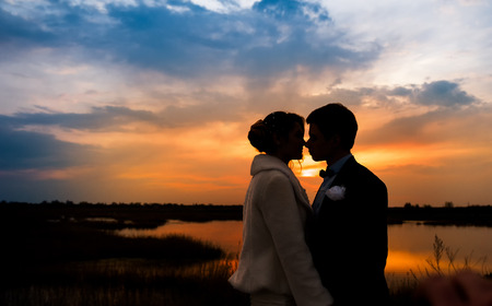 silhouettes of the bride and groom on the background of the setting sun and lake.の写真素材