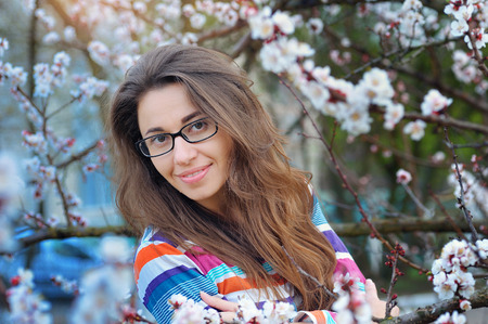 Brunette in glasses on a background of a blossoming tree in spring.