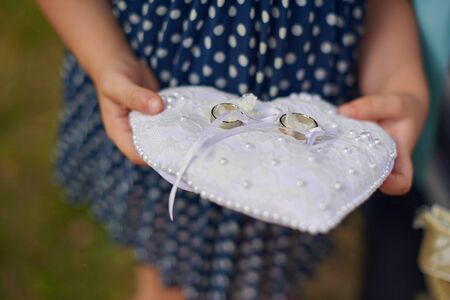 Closeup shot of little girl holding cushion with wedding ringsの写真素材