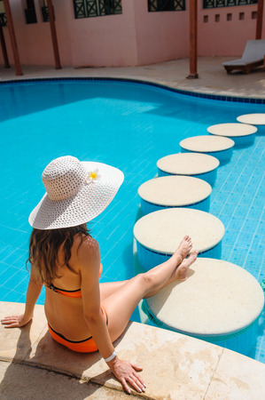beautiful young woman sitting on the edge of the pool.の写真素材