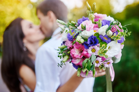 young couple kissing and a girl holding a beautiful bouquet, focus on bouquetの写真素材