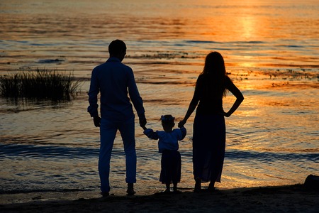 silhouettes of parents and child on the background of the setting sun.の写真素材