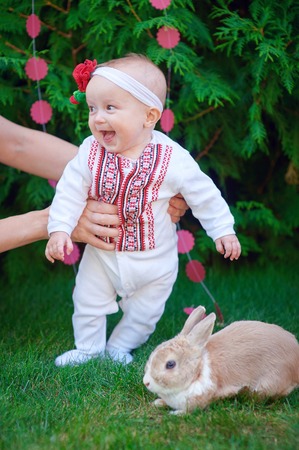 Cute funny happy baby with rabbit making his first steps on a green grass in a sunny summer gardenの写真素材