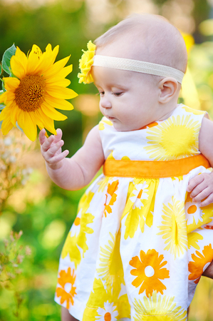 Beautiful little girl in a yellow dress smelling a sunflower.の写真素材