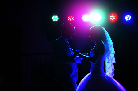 Kiss and dance young bride and groom in dark banqueting hallの写真素材