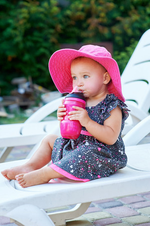 Little baby girl in autumn park drinks from pink plastic bottle.の写真素材