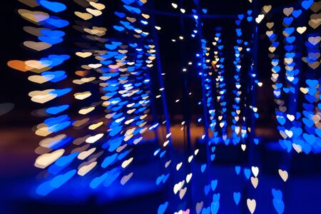 beautiful bokeh made of warm blue blurred lights in the form of hearts on dark backgroundの写真素材