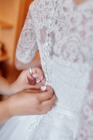 Bridesmaids helping the bride to wear a wedding dress.の写真素材