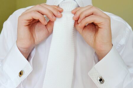 Detail of young businessman correcting a white tie.