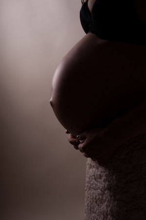 pregnancy, motherhood, people and expectation concept - silhouette of happy pregnant woman with big bare tummy near window at homeの写真素材
