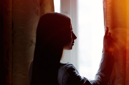 beautiful young woman standing near a window in the room.