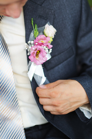 groom adjusts his boutonniere of pink flowers close up.の写真素材