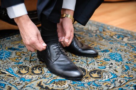 groom ties the laces on black wedding shoes.の写真素材