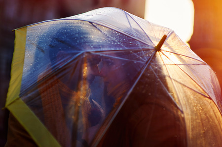 Closeup of young beautiful couple kissing under the umbrella in an autumn rainy dayの写真素材