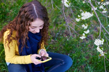 Beautiful young woman sitting on grass with a smartphone.の写真素材