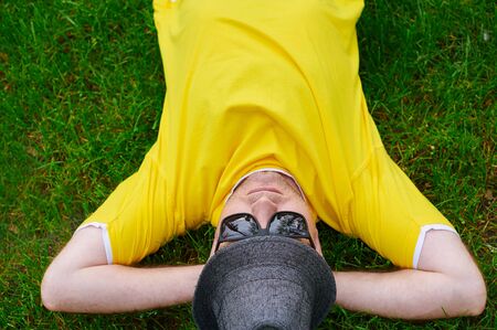 man in a yellow T-shirt and hat lying on the grass.の写真素材
