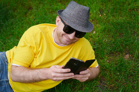 smart young man in a yellow T-shirt with the phone on the grass.の写真素材