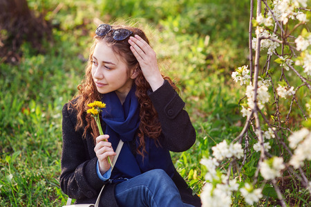 young woman in black coat walking in a blossoming spring garden.の写真素材