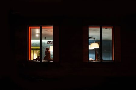 woman sitting in a lighted room near window at night.の写真素材