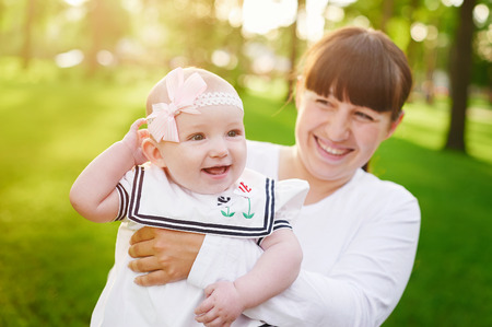 Beautiful lifestyle summer photo mother and baby girl walks in the park, warm sunlight