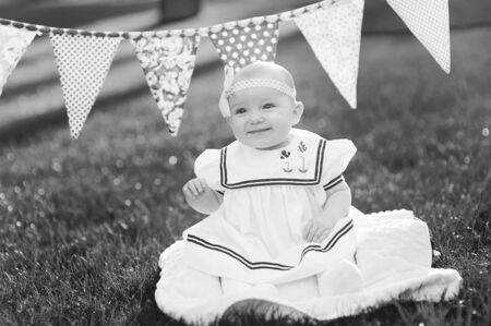 happy little girl sitting on the grass with flags on the background.の写真素材