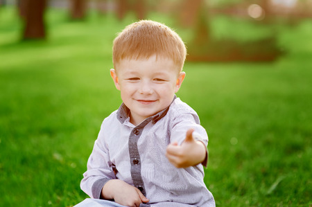 smiling boy sits on the green grass in the summer park.の写真素材