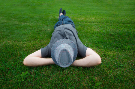 man lying in a field on green grass with the hat over his face.の写真素材