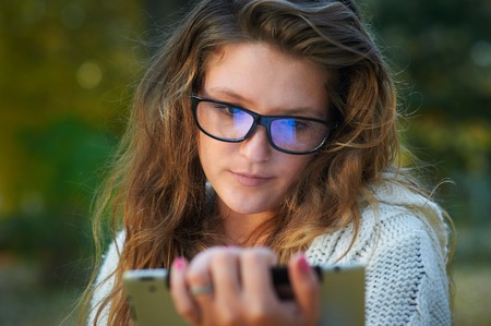 beautiful young woman in glasses with the tablet in the autumn park.の写真素材
