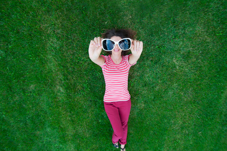 beautiful woman lying on the grass and holding glasses in his hand.の写真素材