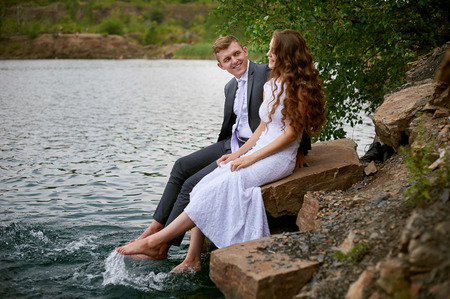 loving wedding couple sitting and kissing near water.
