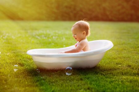 little baby girl bathes in bath on meadowの写真素材